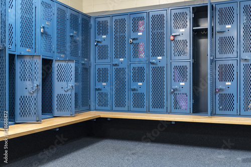Blue metal cage lockers in a locker room with some doors open and some closed with a wooden bench