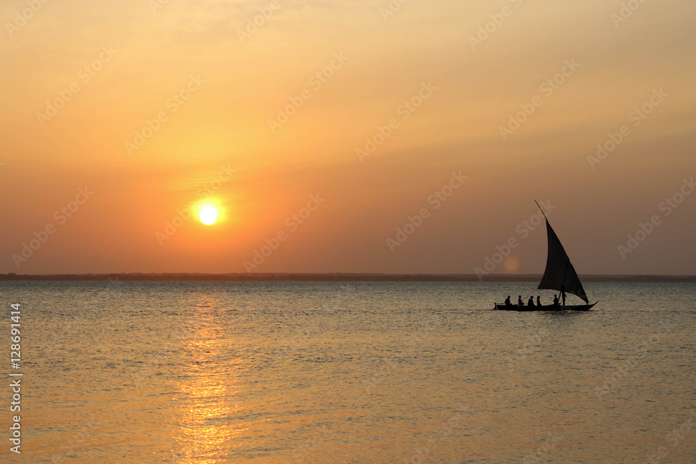 Sunset over the ocean with a sail boat heading toward the right side