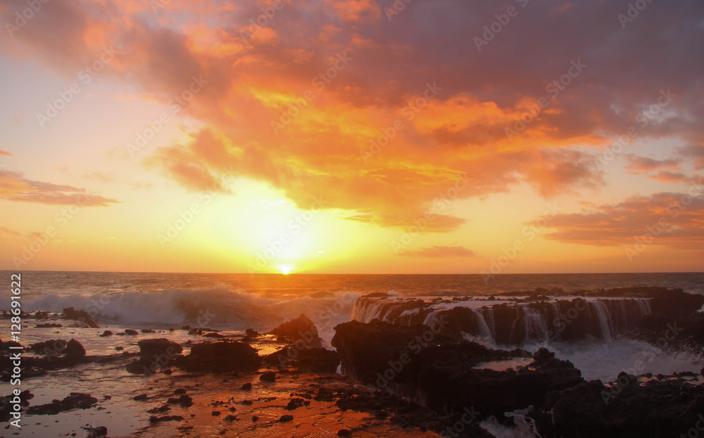 Sunset over the ocean with water-covered rocks in foreground, bright clouds above