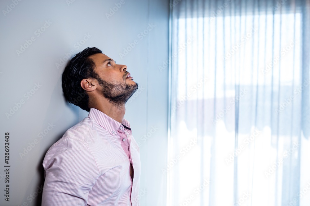 Businessman standing against wall and looking up Businessman standing against wall and looking up