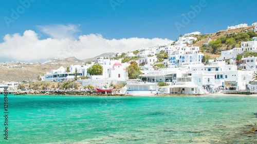 Vibrant Scene of Mykonos Island in Greece with White Buildings against Turquoise Blue Mediterranean Sea Water during Perfect Weather