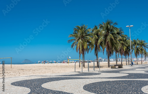 Copacabana beach with white sand, blue sky, green palms and mosaic floor, black and white Portuguese pavement in Rio de Janeiro, Brazil photo