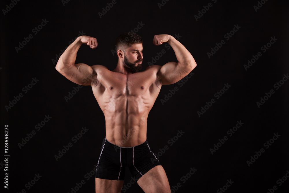 Rear view of healthy muscular young man with his arms stretched out isolated on black background