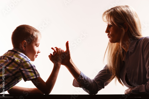 Mother and son arm wrestle sit at table.