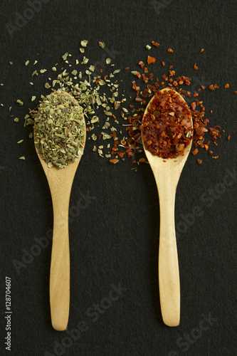 Two spoons with red pepper and green dry herbs