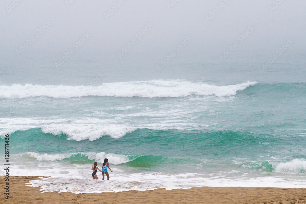 Two little girls running around and playing on the ocean.