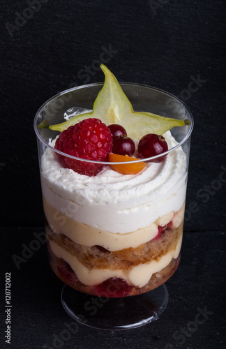 Small snacks trifle with fruits and cream in plastic glass on a