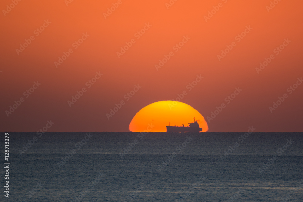 Silhouette of a ship at the horizon while the sun sets down behind