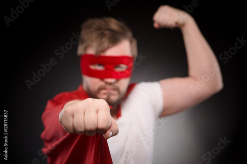 Image of super hero man showing wrist while posing for photographer in studio. Handsome man in red mask ready to save world and help people.