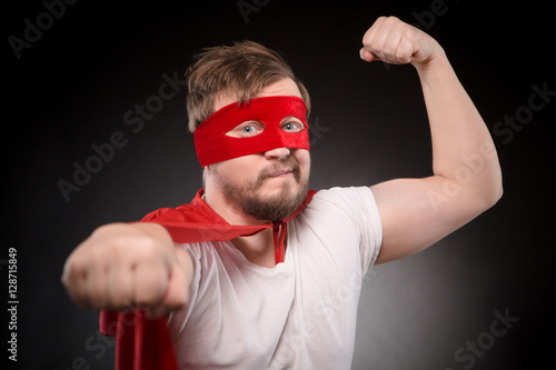 Portrait of funny super hero mn with red msk on showing his strength or force isolated on black background. Handsome man showing his wrist in studio. photo