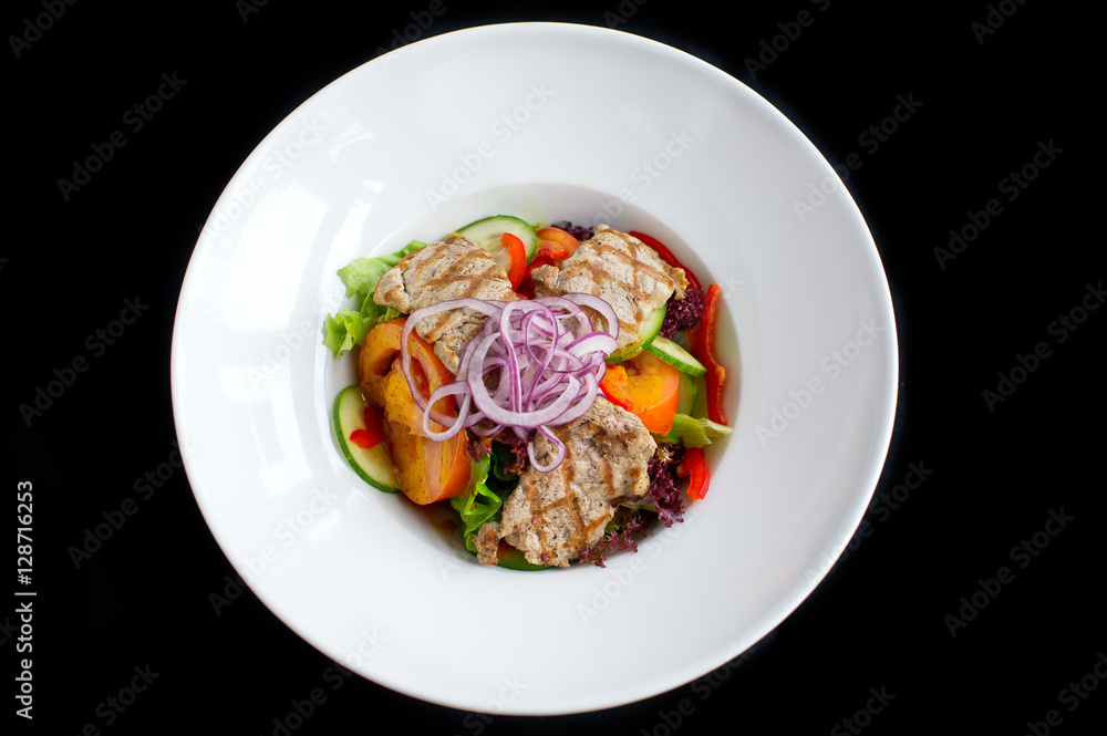 salad with grilled pork and fresh vegetables in white plate and black background