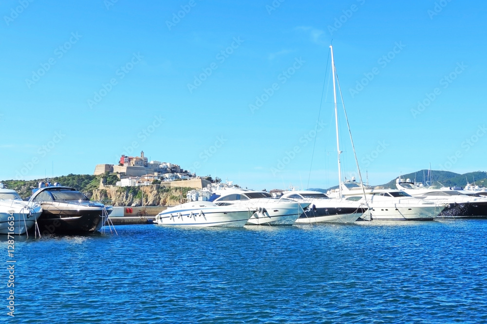 Yacht harbor of Ibiza town with anchored yachts and sailing ships in the sun.