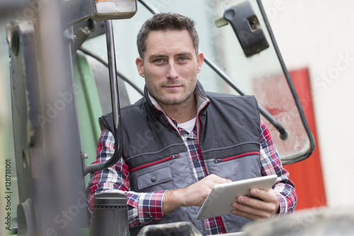 Slika na platnu Farmer leaning on the tractor using a digital tablet