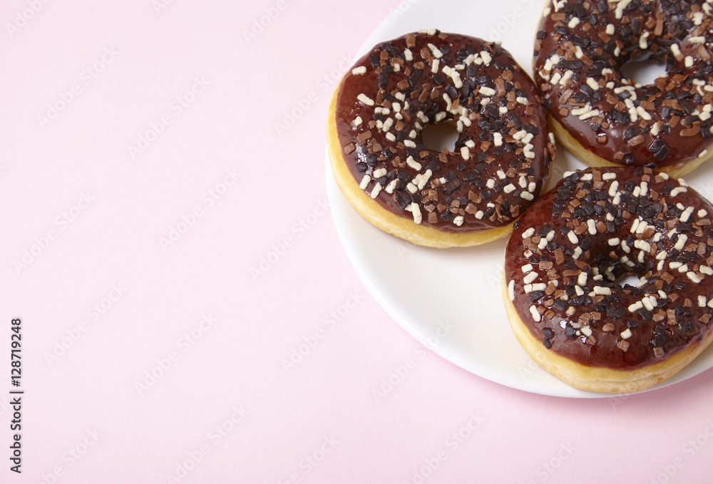 A plate full of iced chocolate sprinkle ring donuts on a pastel pink background with blank space at side A plate full of iced chocolate sprinkle ring donuts on a pastel pink background with blank space at side