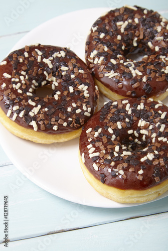 A close up of a plate full of iced chocolate sprinkle ring donuts on a painted wooden background