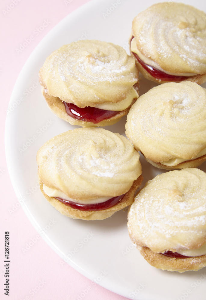A close up of a plate full of freshly baked Viennese whirl biscuits on a pastel pink background