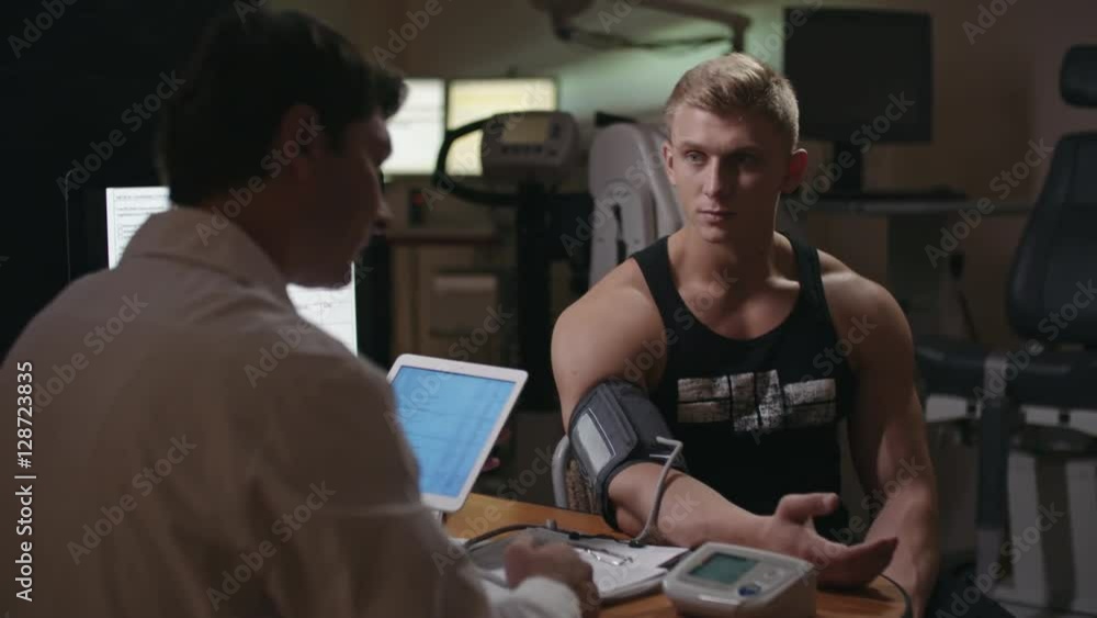 Doctor performing blood pressure checkup and explaining results to muscly patient Doctor performing blood pressure checkup and explaining results to muscly patient