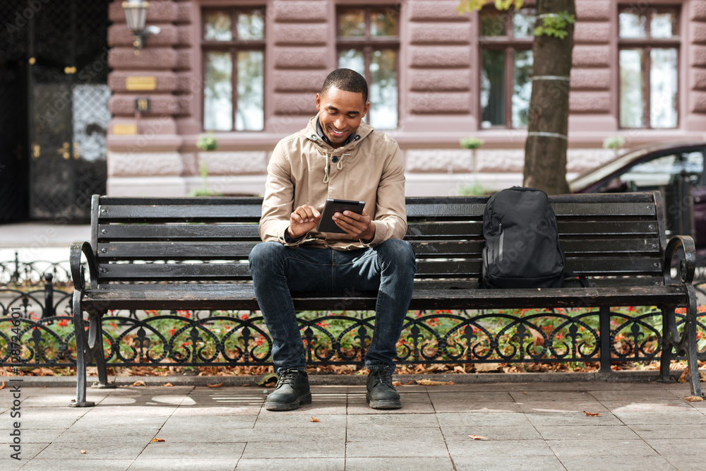 Man with tablet sitting on bench near backpack and typing Man with tablet sitting on bench near backpack and typing
