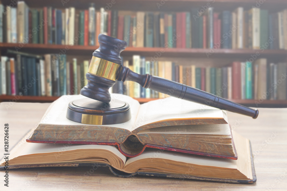 Wooden Law Gavel on open books with a row of law books in library Wooden Law Gavel on open books with a row of law books in library