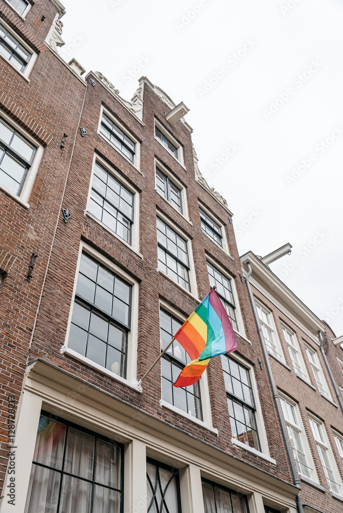 Gay Pride flag in a building in Amsterdam, low angle view against cloudy sky