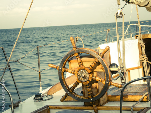 Steering wheel on the old sailboat. Sea voyage of the sailing vessel. Travel at sail boat with a wooden helm in front. Ship wheel on the old yacht - nautical equipment closeup.
