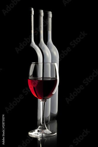 Elegant red wine glass and a wine bottles in black background.