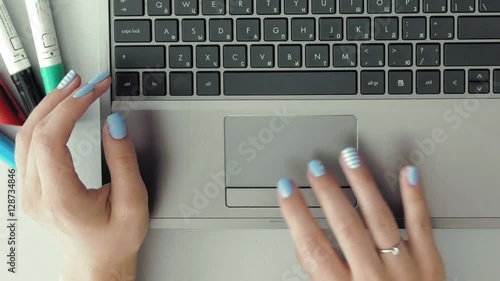 Female hands with colorful nails working on her laptop. POV from first person. The smartphone paper cap and highlighters are shown on her desk. Modern computer technology applies to everybody.