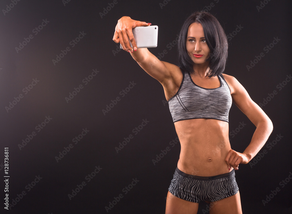 Sports, fitness, bodybuilding concepts. Bodybuilder woman posing with her  hand on hip and holding mobile or smart phone in front of her. Pretty  fitness lady making self photos. Photos | Adobe Stock