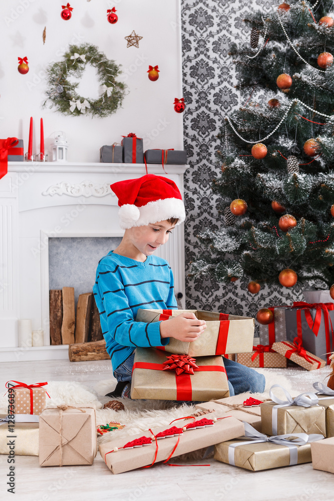 Cute boy in santa hat unwrapping christmas presents Cute boy in santa hat unwrapping christmas presents