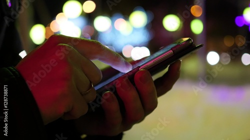 Man sms texting using app on smartphone at night in city, winter time. closeup