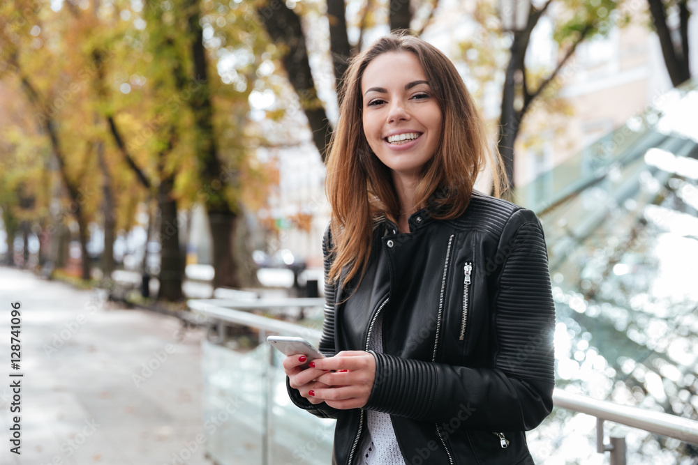 Cheerful woman standing and using smartphone in the city Cheerful woman standing and using smartphone in the city