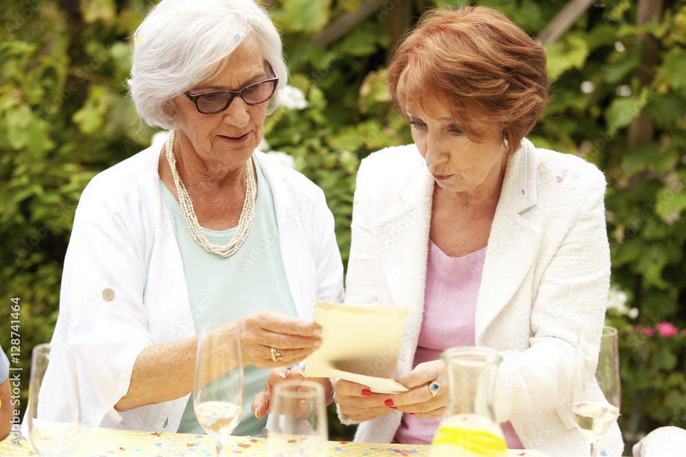 Two senior women looking at photographs at party Two senior women looking at photographs at party