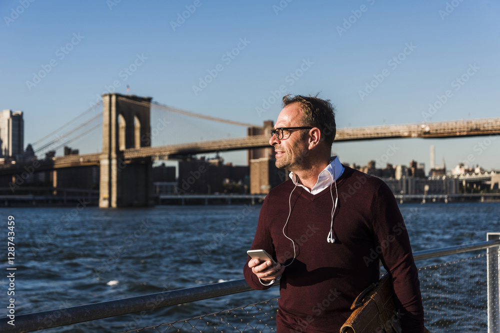 USA, Brooklyn, businessman with smartphone in front of Brooklyn Bridge USA, Brooklyn, businessman with smartphone in front of Brooklyn Bridge