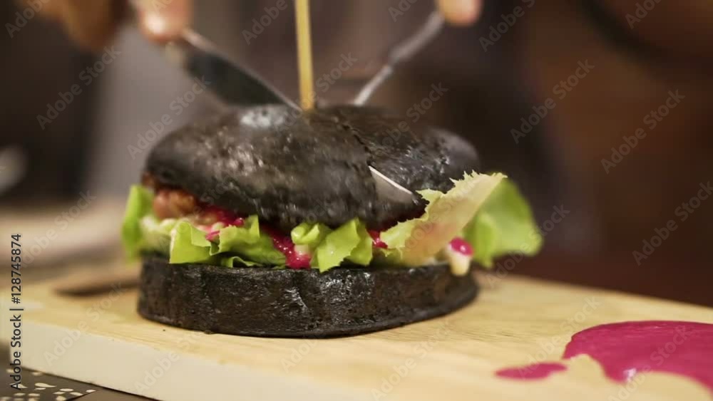 Black charcoal burger with red sauce being cut. New trend healthy black food Black charcoal burger with red sauce being cut. New trend healthy black food