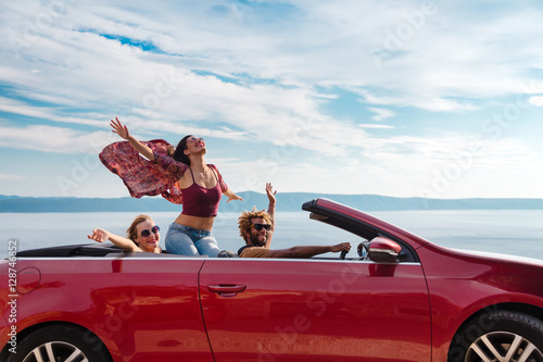 Group of happy young people waving from the red convertible. photo
