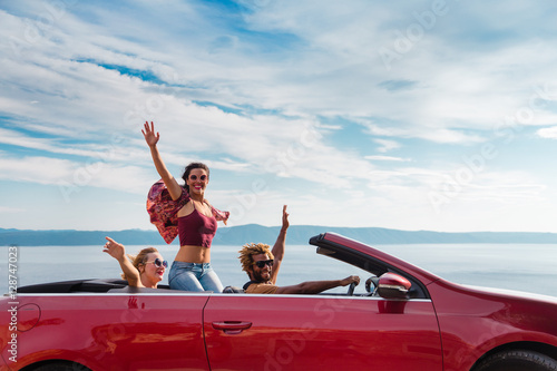 Group of happy young people waving from the red convertible.