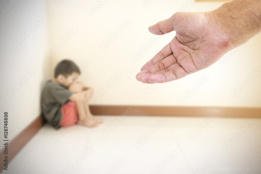 Closeup hand are extended to the boy hugged her knees in tears in a corner of the room. Closeup hand are extended to the boy hugged her knees in tears in a corner of the room.