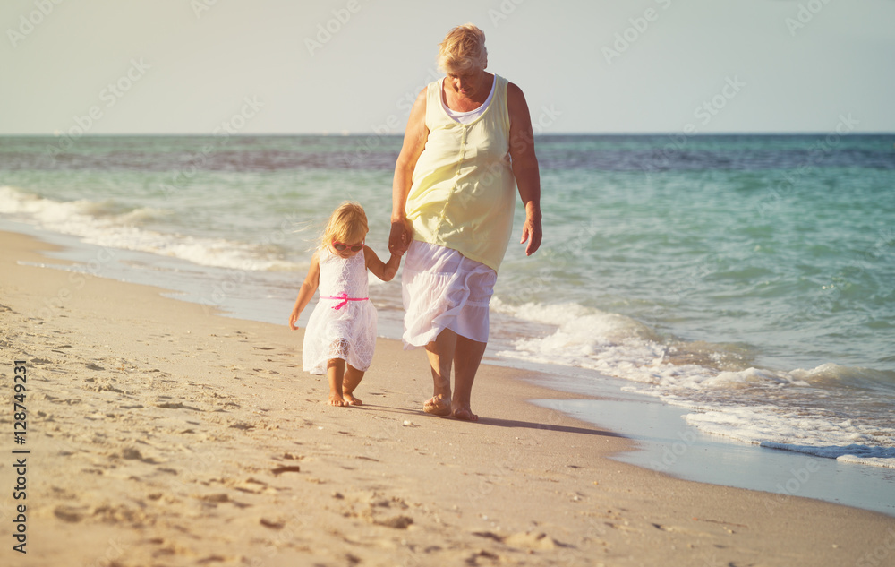 Happy grandmother with little girl walk at beach