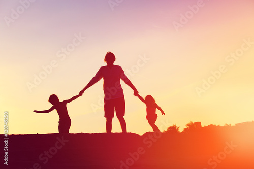 father with son and daughter silhouettes play at sunset