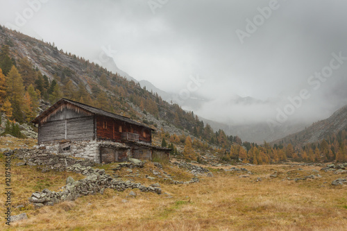 An old closed cowshed at fall in front of a mountain meadow