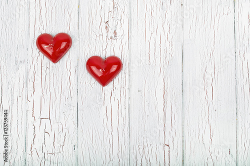 two red hearts lie on a white wooden surface