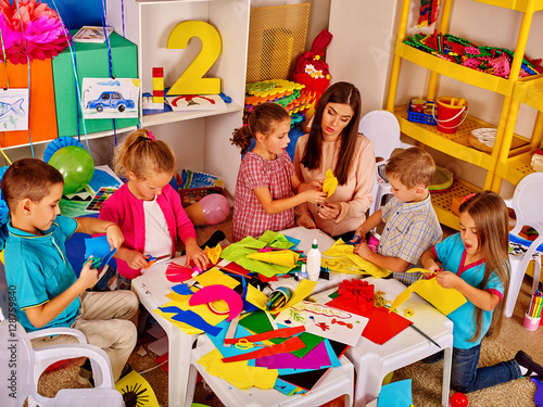 Large group of children with the teacher in a kindergarten. Children create crafts out of colored paper.