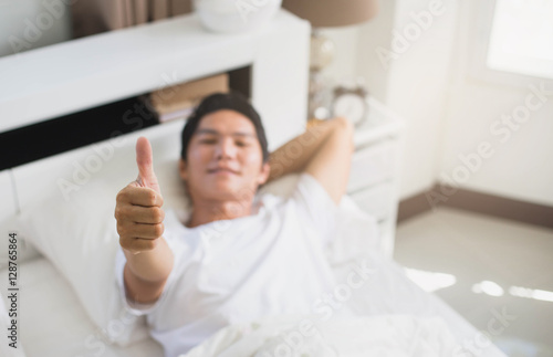 Young man with thumbs up in his white bedroom.