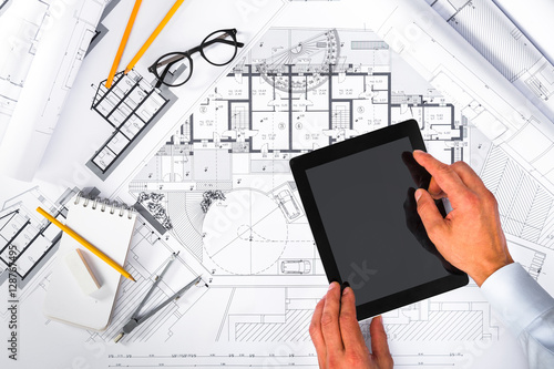 Construction plans and Male Hands using a Tablet on blueprints;