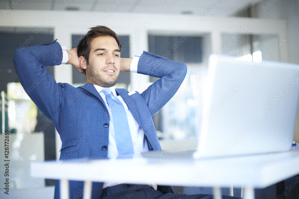 Shot of a satisfied young businessman with hands on nape sitting in the office in front of his laptop after a well done job. Shot of a satisfied young businessman with hands on nape sitting in the office in front of his laptop after a well done job.