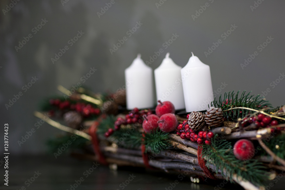 Christmas white candles on a bunch of twigs decorated with fir cones and berries on a gray background