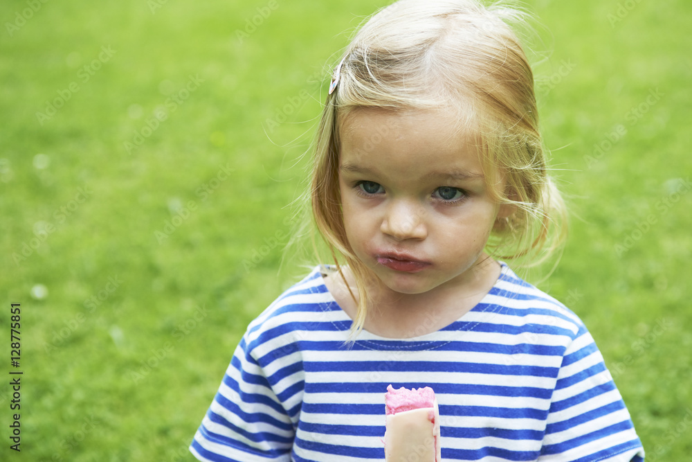 Beautiful little girl eats ice-cream in the summer with green grass background.
Beautiful little girl eats ice-cream in the summer with green grass background.