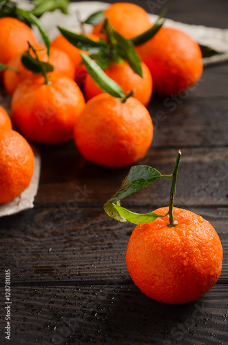 Fresh tangerine clementine with leaves on dark wooden background, selective focus, vertical.