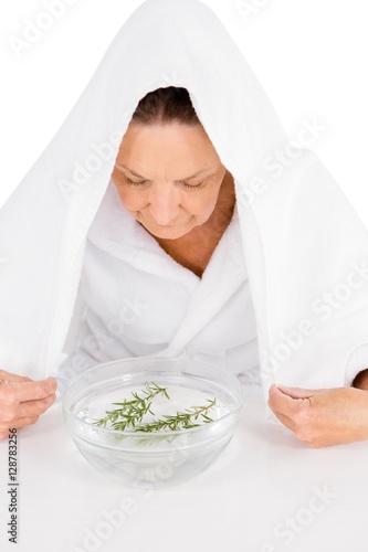 Mature woman steaming face with rosemary in bowl of water