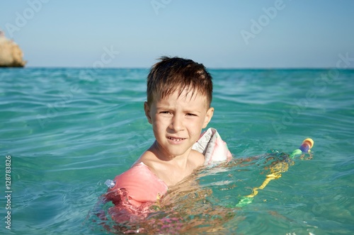 Schilderij op canvas Boy with floater  sleeves swimming in a sea and having fun with water pistol